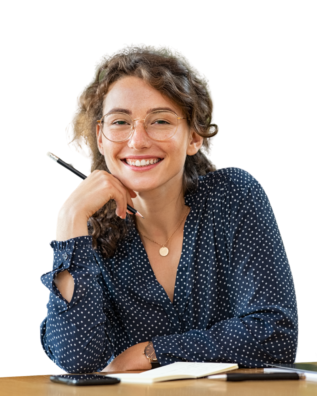 Vrolijk meisje met licht bruin gekruld haar heeft een bril op en een potlood in haar hand. Ze leunt op een tafel en heeft een blauwe blouse met witte stippen aan.